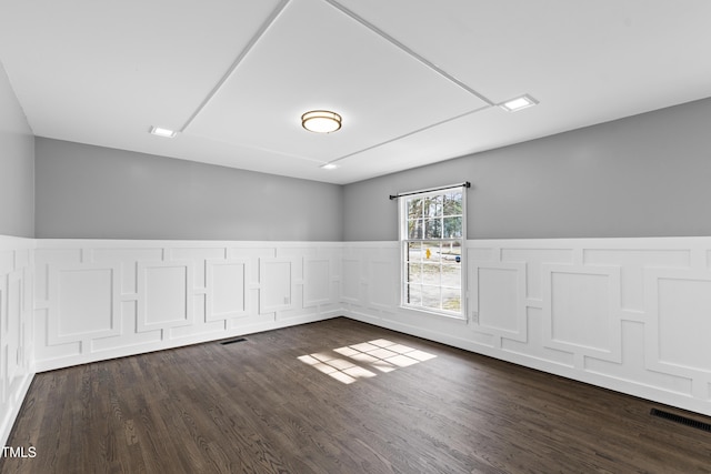 spare room featuring dark wood-style floors, wainscoting, and visible vents