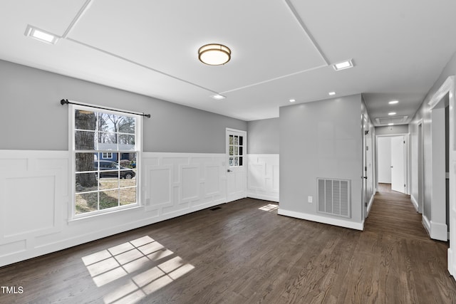 unfurnished room featuring a wealth of natural light, visible vents, dark wood-type flooring, and wainscoting