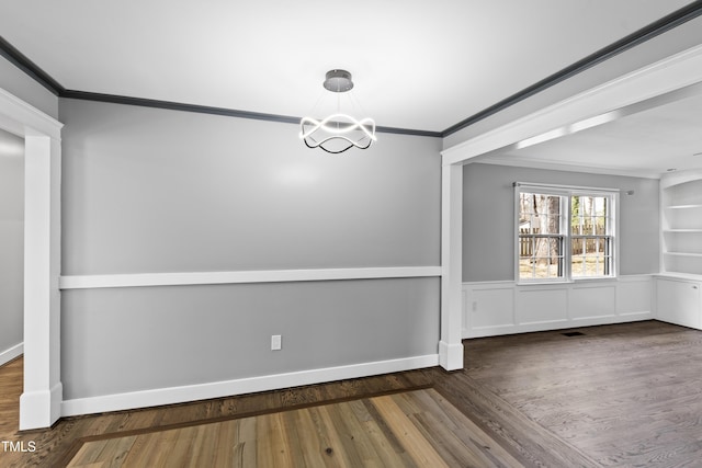 unfurnished dining area with baseboards, ornamental molding, a chandelier, and wood finished floors