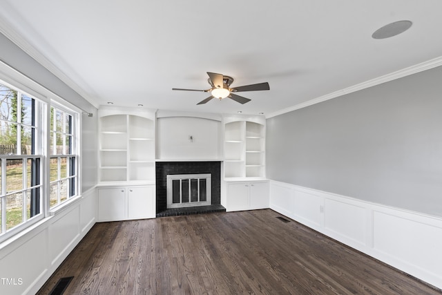 unfurnished living room with built in shelves, a fireplace, visible vents, dark wood finished floors, and crown molding