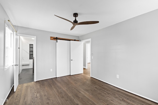 unfurnished bedroom with ceiling fan, a barn door, wood finished floors, a closet, and ensuite bath