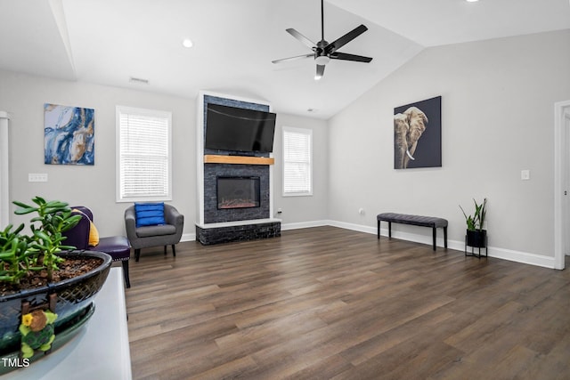 living area featuring lofted ceiling, a ceiling fan, a large fireplace, wood finished floors, and baseboards