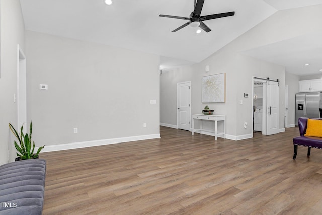 living area with a barn door, a ceiling fan, baseboards, vaulted ceiling, and light wood-style floors