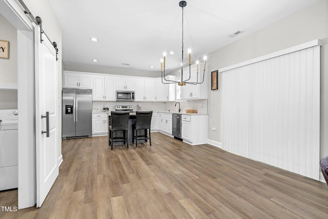 kitchen with washer / dryer, a barn door, white cabinets, appliances with stainless steel finishes, and a sink