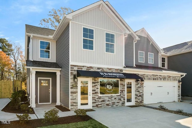 view of front of home featuring concrete driveway, an attached garage, board and batten siding, fence, and stone siding