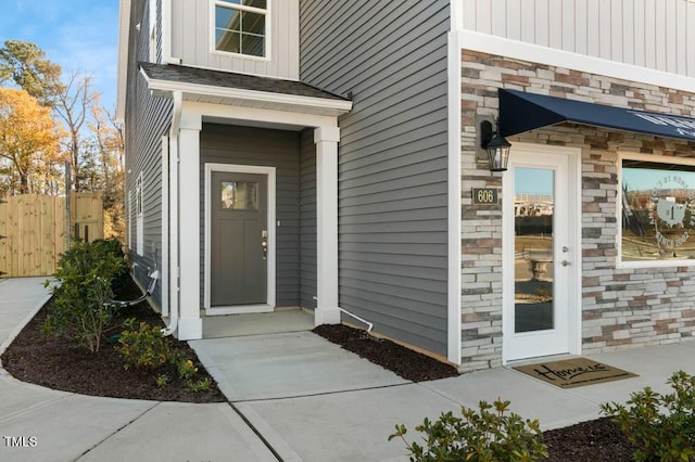 view of exterior entry with board and batten siding, stone siding, and fence