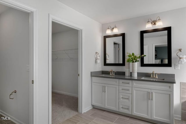 full bathroom with double vanity, a sink, a walk in closet, and baseboards