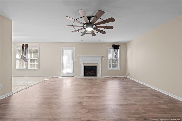 unfurnished living room with ceiling fan, baseboards, wood finished floors, and a fireplace with flush hearth