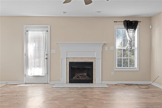 unfurnished living room with a tiled fireplace, wood finished floors, a ceiling fan, and baseboards