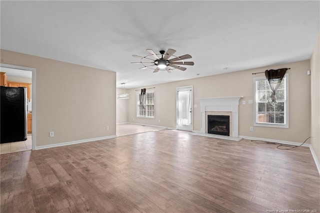 unfurnished living room with light wood finished floors, baseboards, a ceiling fan, and a tile fireplace