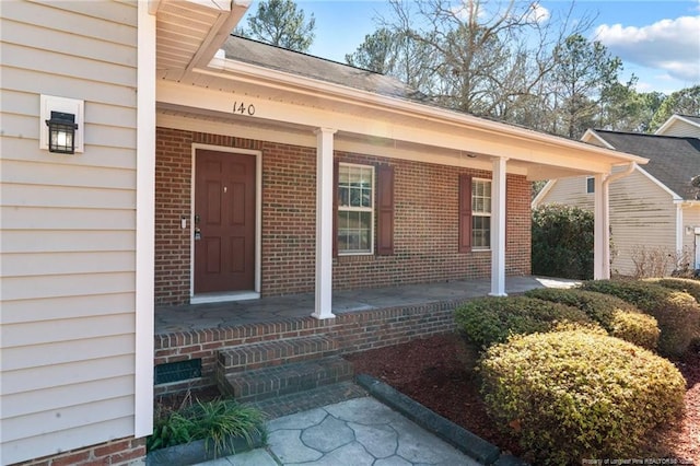 doorway to property featuring a porch and brick siding