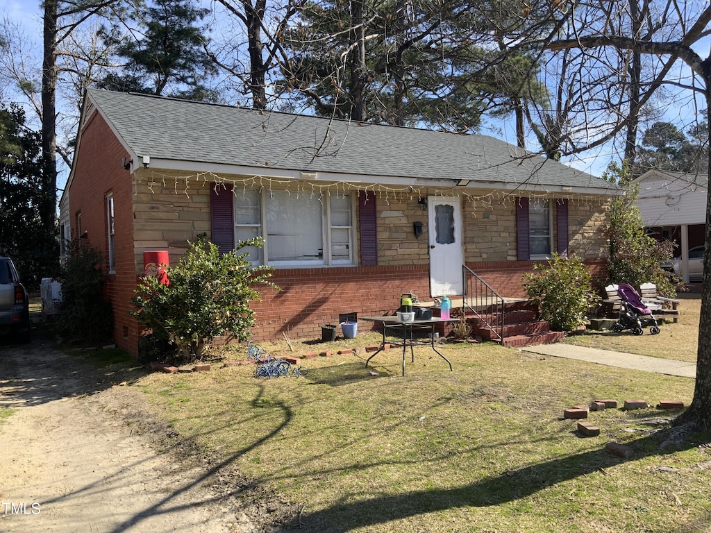 view of front of house featuring stone siding, roof with shingles, a front yard, and brick siding