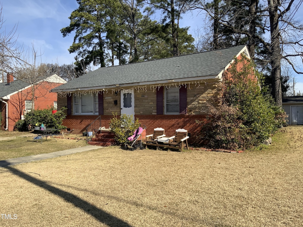 single story home with stone siding, roof with shingles, a front yard, and brick siding