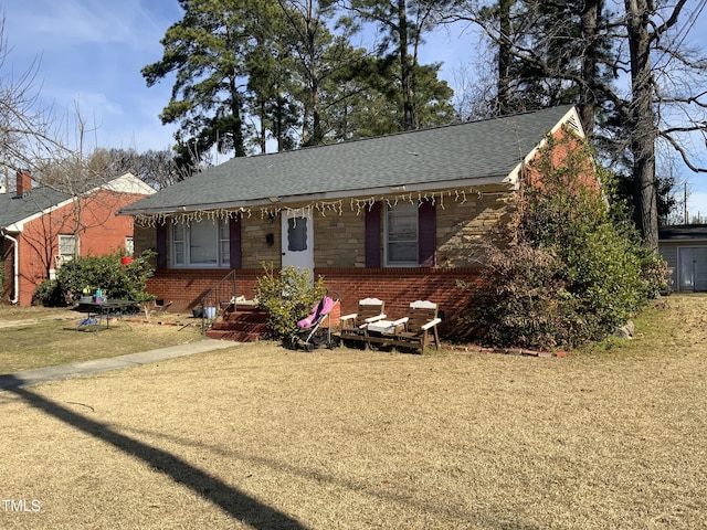 single story home with stone siding, roof with shingles, a front yard, and brick siding