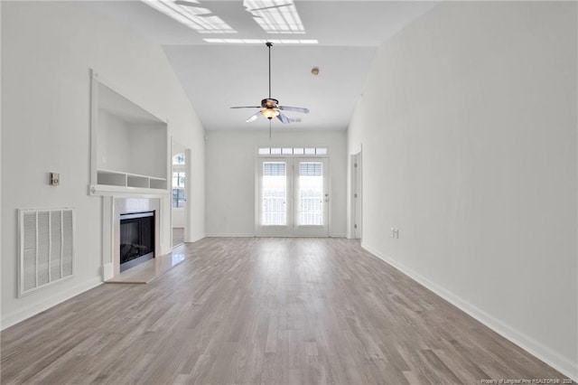 unfurnished living room featuring baseboards, visible vents, a fireplace with raised hearth, ceiling fan, and wood finished floors