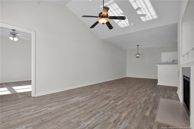 unfurnished living room with lofted ceiling, a fireplace with flush hearth, wood finished floors, a ceiling fan, and baseboards