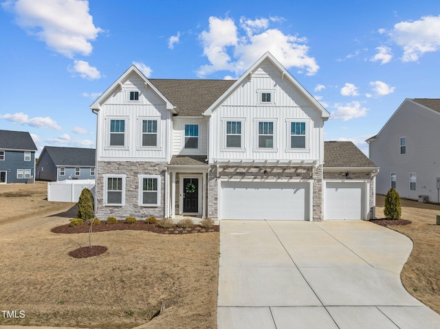 view of front of home with driveway, a garage, stone siding, fence, and board and batten siding