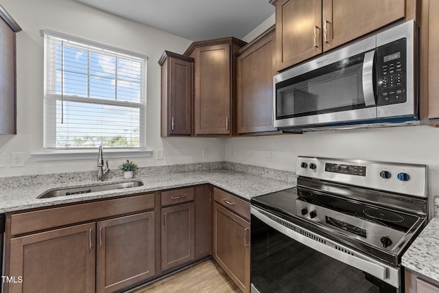 kitchen featuring light wood-type flooring, light stone counters, stainless steel appliances, and a sink