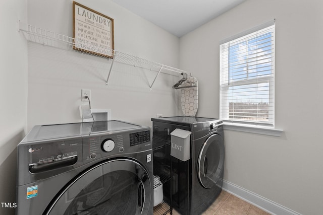 clothes washing area with laundry area, washing machine and dryer, light tile patterned floors, and baseboards