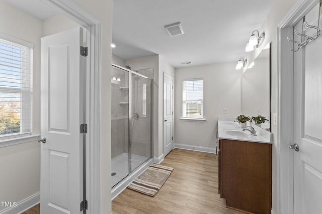 bathroom featuring double vanity, visible vents, a sink, a shower stall, and wood finished floors