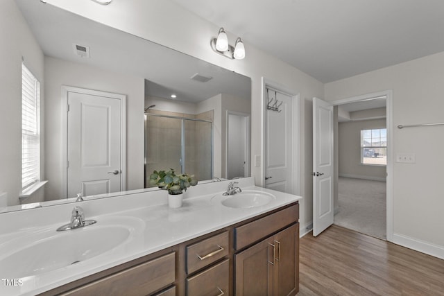 full bathroom with double vanity, a shower stall, a sink, and wood finished floors