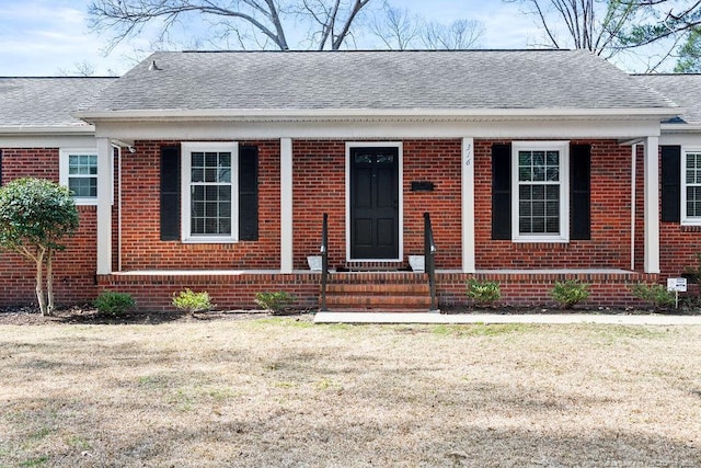 view of front facade featuring a shingled roof, a front yard, and brick siding