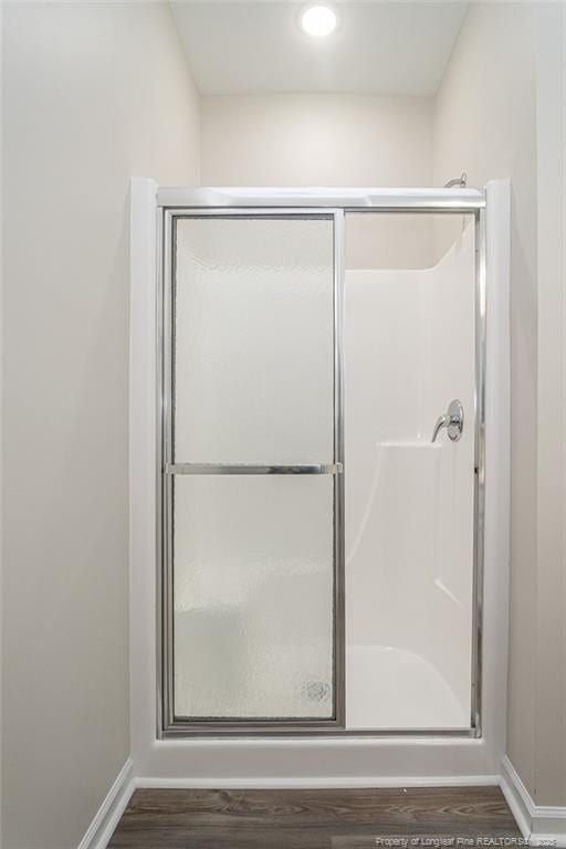 full bathroom with wood finished floors, a shower stall, and baseboards