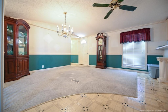 carpeted spare room featuring a textured ceiling, ceiling fan with notable chandelier, visible vents, and baseboards