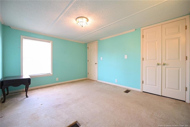 carpeted empty room featuring visible vents, baseboards, a textured ceiling, and ornamental molding