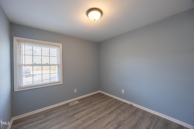 empty room with wood finished floors, visible vents, and baseboards