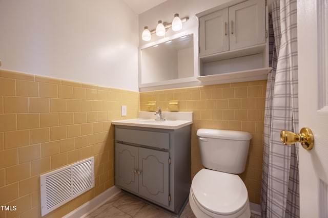 bathroom featuring a wainscoted wall, tile walls, visible vents, toilet, and vanity