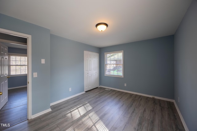 unfurnished bedroom featuring a closet, multiple windows, baseboards, and wood finished floors