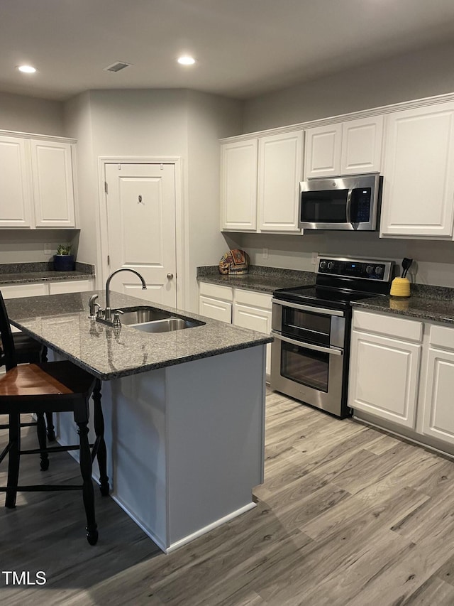 kitchen with light wood-style flooring, a sink, white cabinetry, a kitchen breakfast bar, and appliances with stainless steel finishes