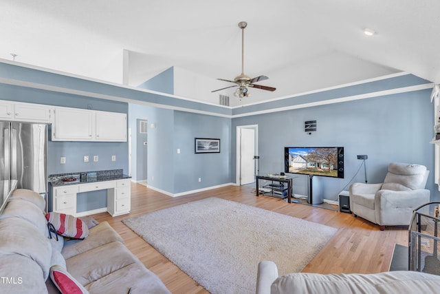 living area featuring baseboards, a raised ceiling, lofted ceiling, light wood-style flooring, and built in desk