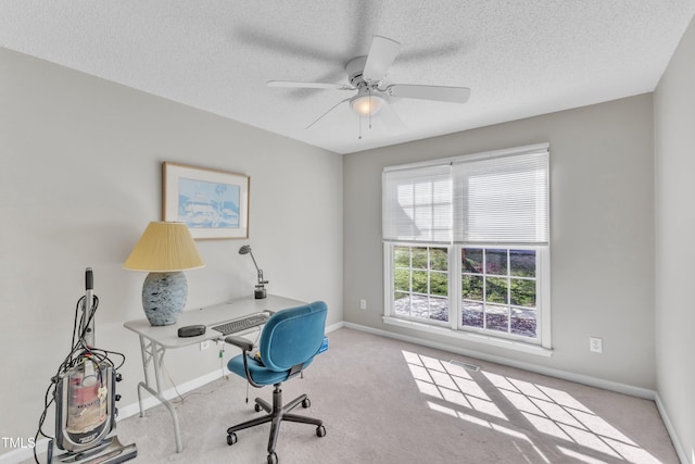 carpeted office space with ceiling fan, baseboards, and a textured ceiling