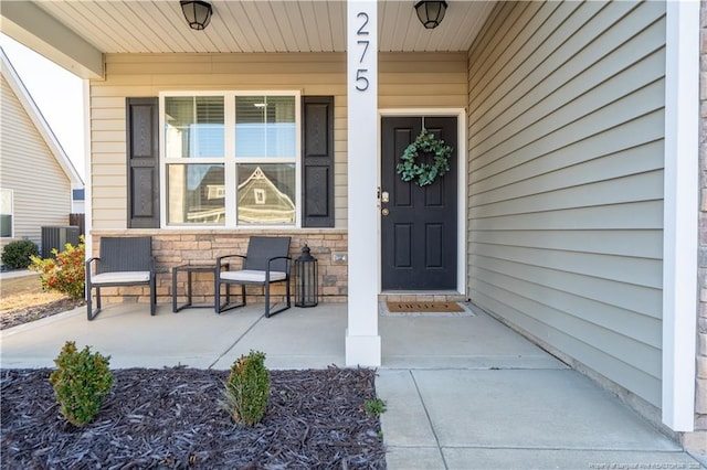 doorway to property with a porch, stone siding, and central AC unit