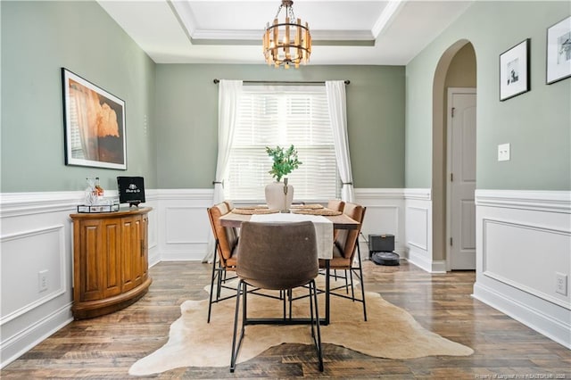 dining room featuring arched walkways, a raised ceiling, wood finished floors, and a chandelier