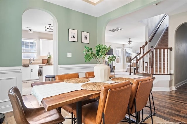 dining room with arched walkways, a wainscoted wall, visible vents, stairway, and wood finished floors