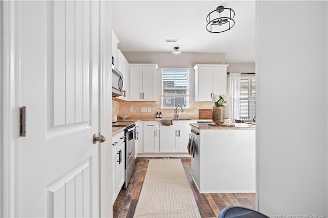 kitchen featuring dark wood-style flooring, stainless steel appliances, backsplash, white cabinetry, and a sink