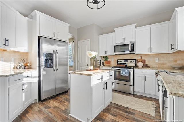 kitchen featuring arched walkways, white cabinets, decorative backsplash, dark wood finished floors, and stainless steel appliances