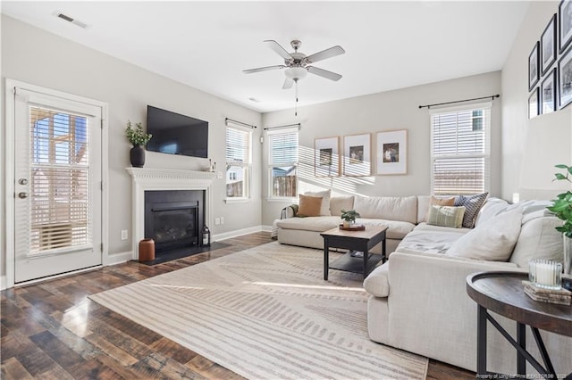 living area featuring a fireplace with flush hearth, a ceiling fan, wood finished floors, visible vents, and baseboards