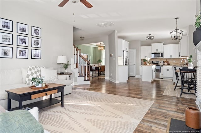 living area featuring baseboards, stairway, wood finished floors, and ceiling fan with notable chandelier