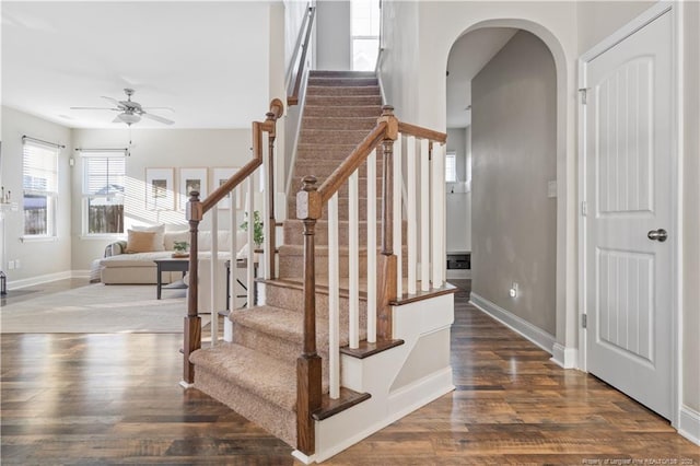 staircase featuring arched walkways, ceiling fan, baseboards, and wood finished floors