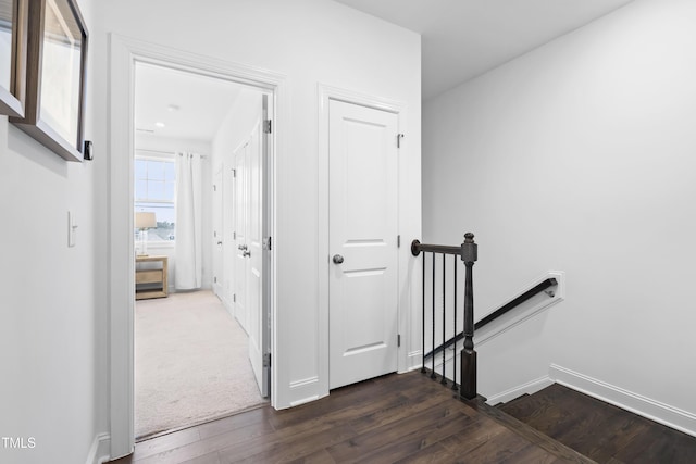 corridor with baseboards, dark wood finished floors, and an upstairs landing