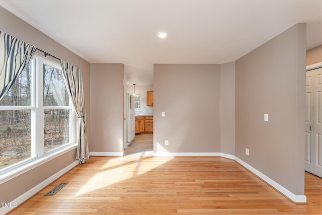 unfurnished room with a wealth of natural light, baseboards, visible vents, and light wood finished floors