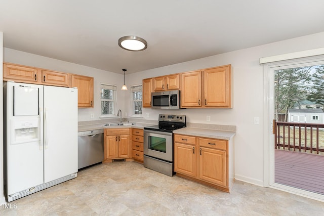 kitchen featuring appliances with stainless steel finishes, light countertops, light brown cabinetry, pendant lighting, and a sink