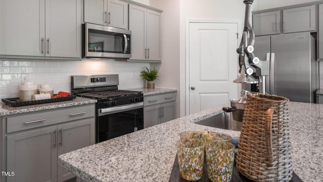 kitchen featuring stainless steel appliances, light stone counters, backsplash, and gray cabinetry