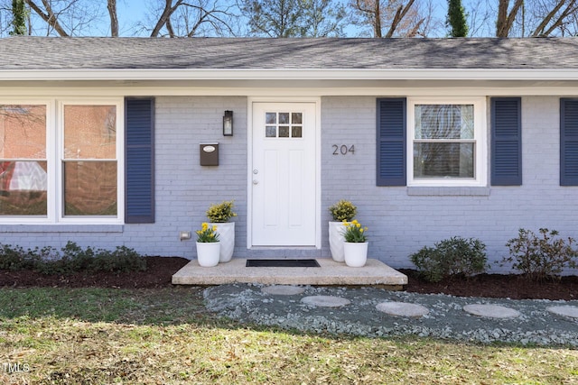 entrance to property featuring roof with shingles and brick siding