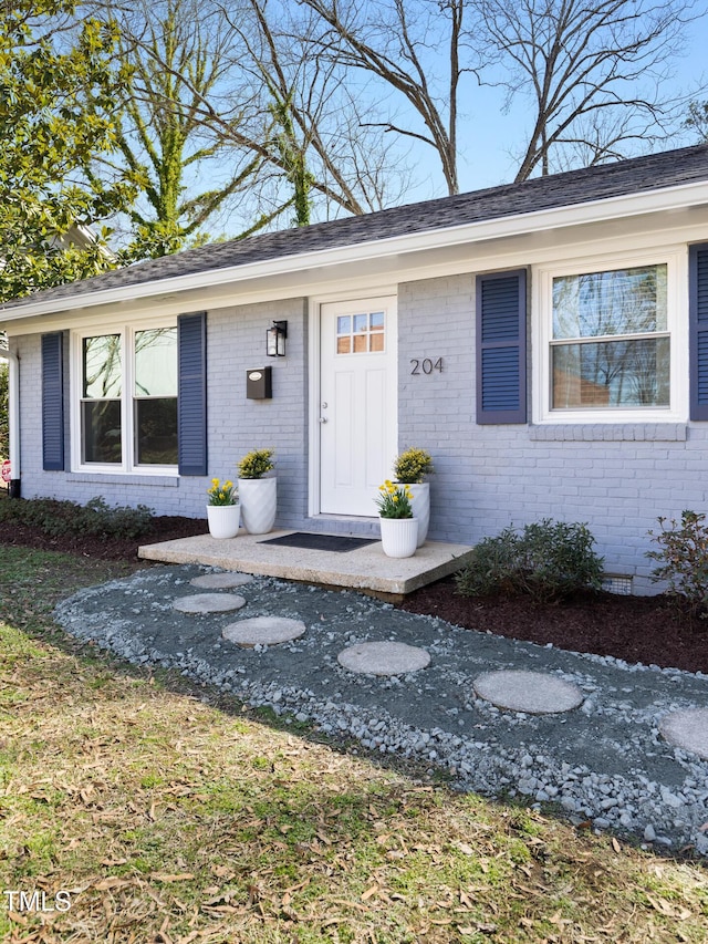 property entrance featuring a shingled roof, crawl space, and brick siding