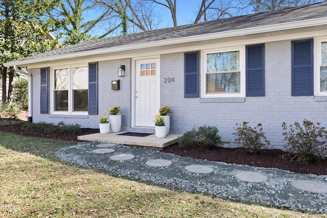 view of exterior entry with crawl space, a shingled roof, and brick siding